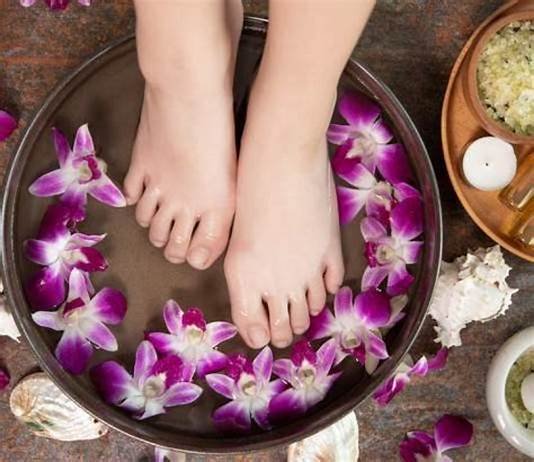a person's feet in a bowl of water with flowers